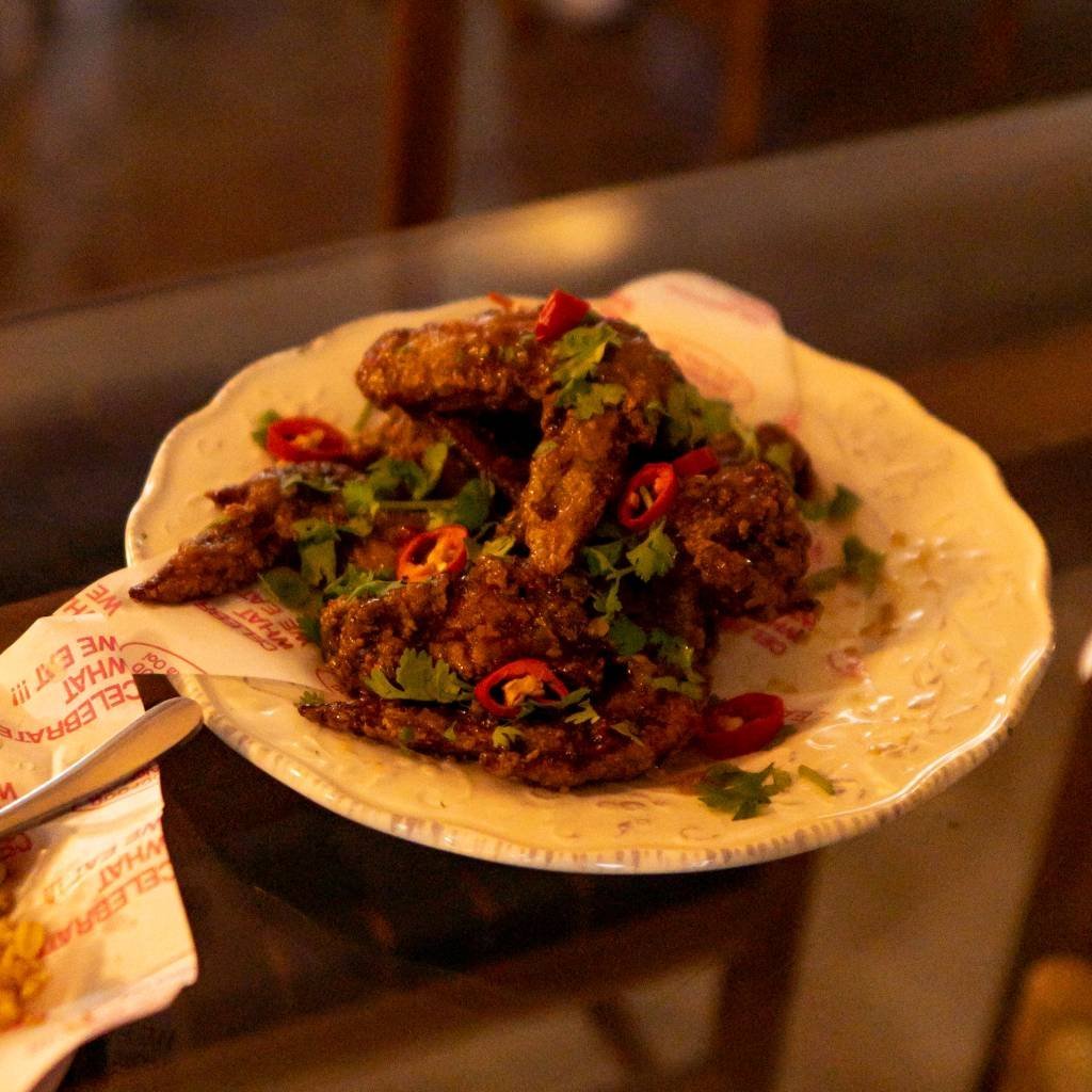 Fried chicken with sticky chilli glaze, coriander and red chilli on paper printed WHAT IF WE CELEBRATE