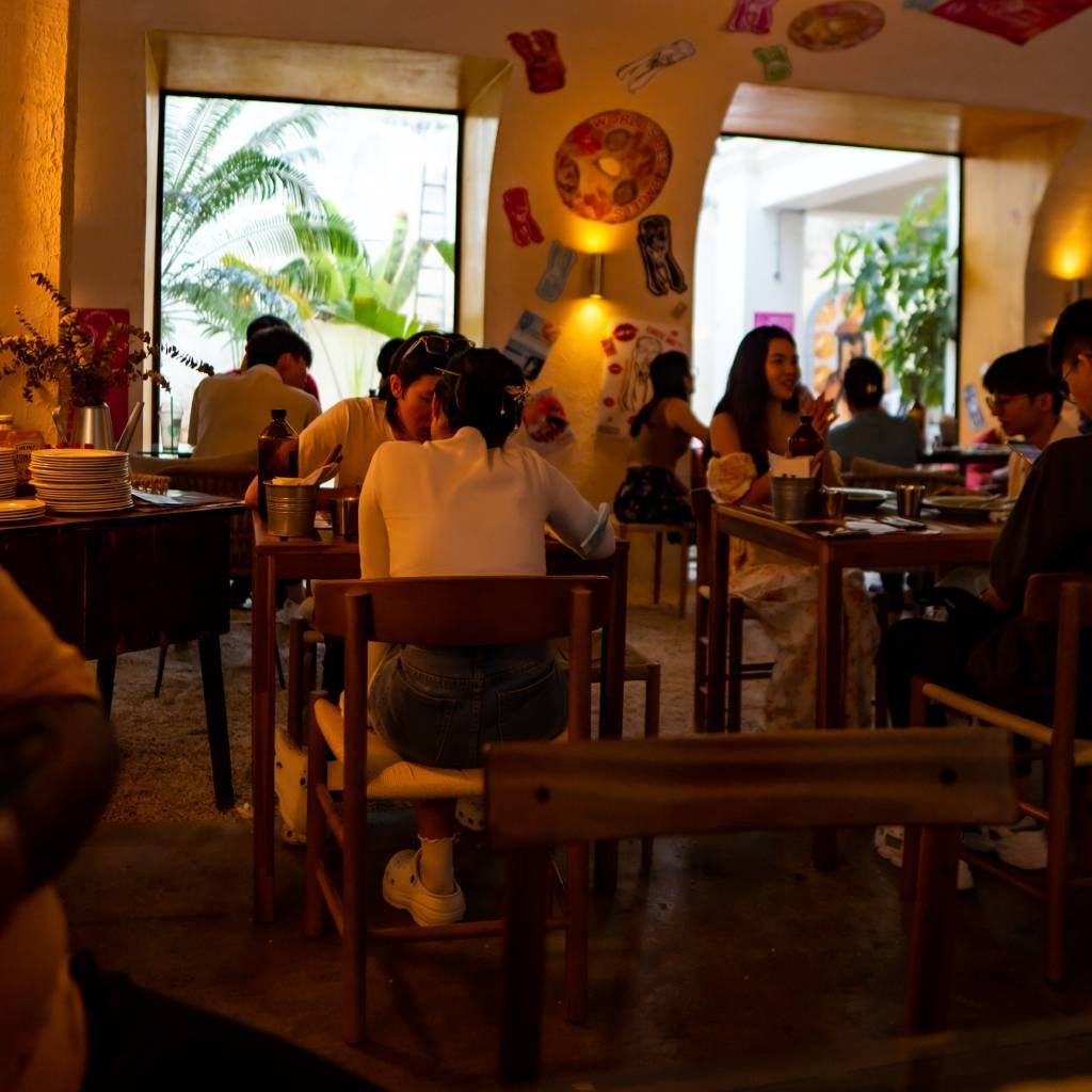 Warm, busy interior of The FOUNDERS Hutton in the afternoon with a sand floor, wooden tables and plaster arches