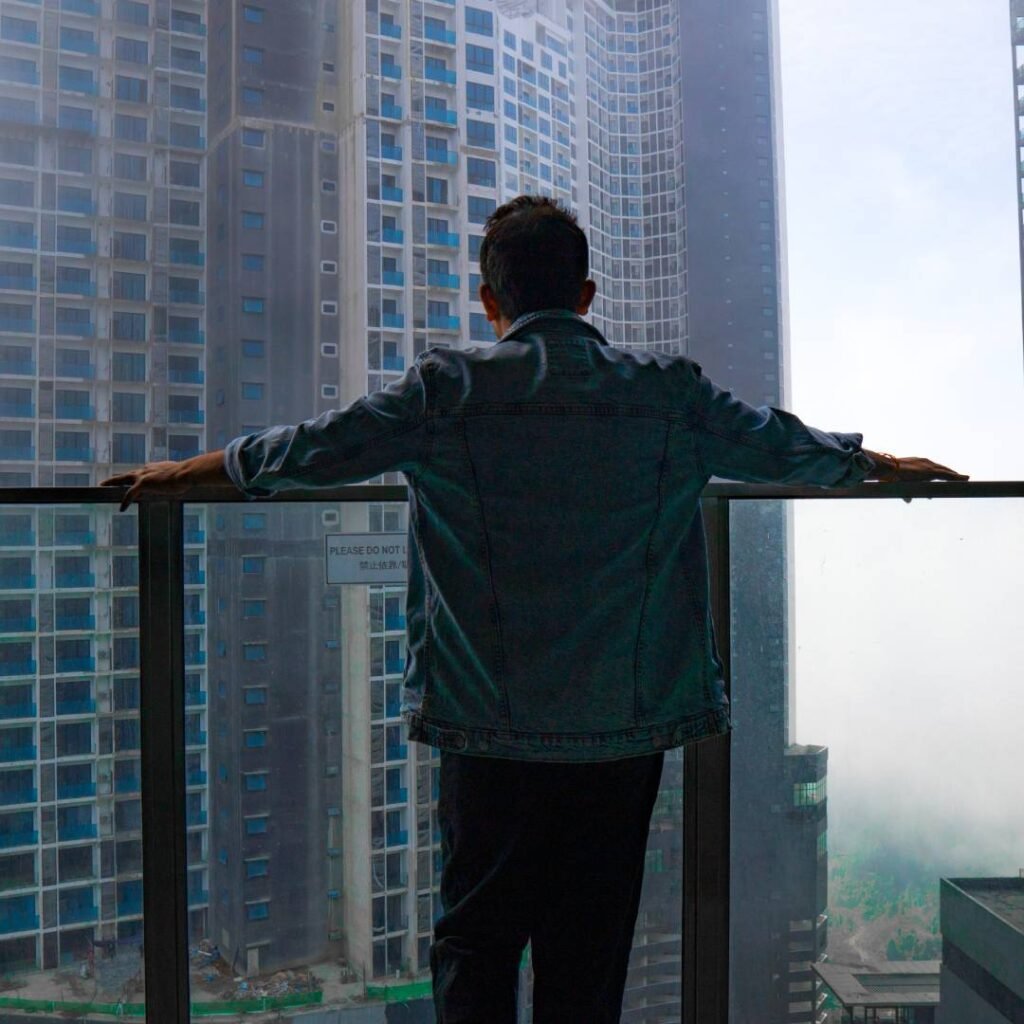Traveller standing on a hotel balcony in Genting Highlands, looking at tall hotel towers in the mist